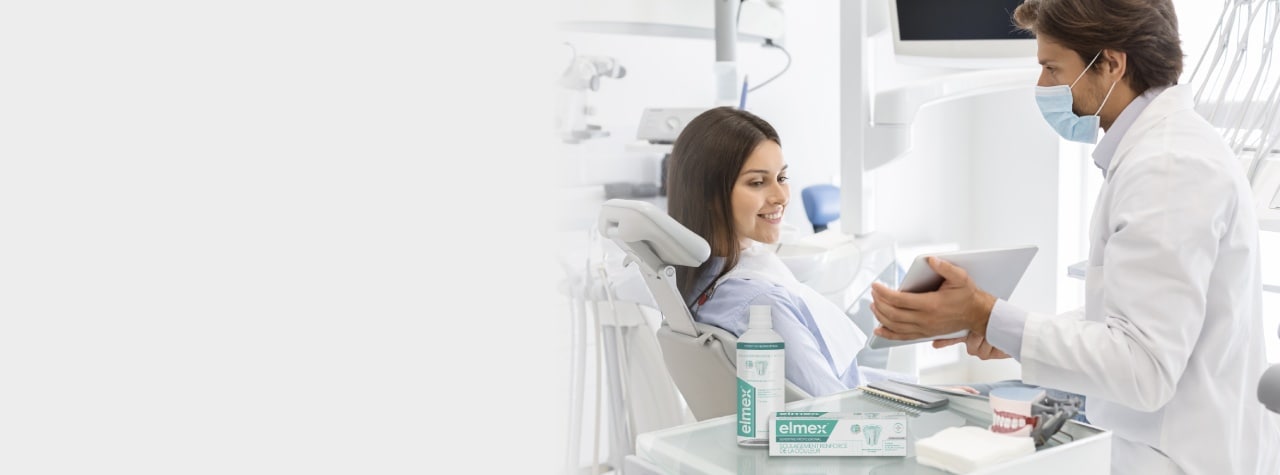 A dental professional wearing safety PPE gear and white lab coat smiling compassionately